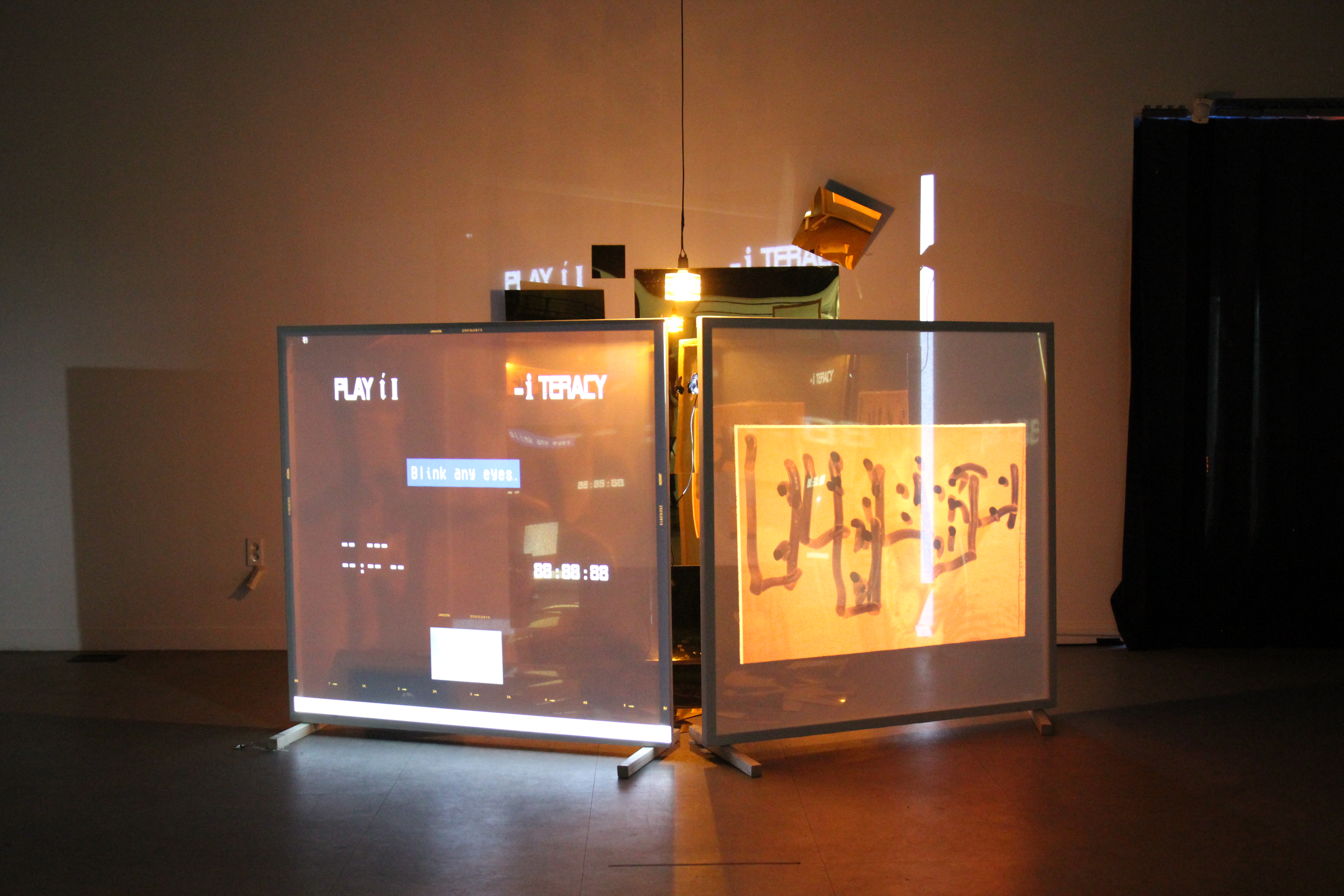 Two screens display projections of scrambled text, lit from behind by reflective metal and light 