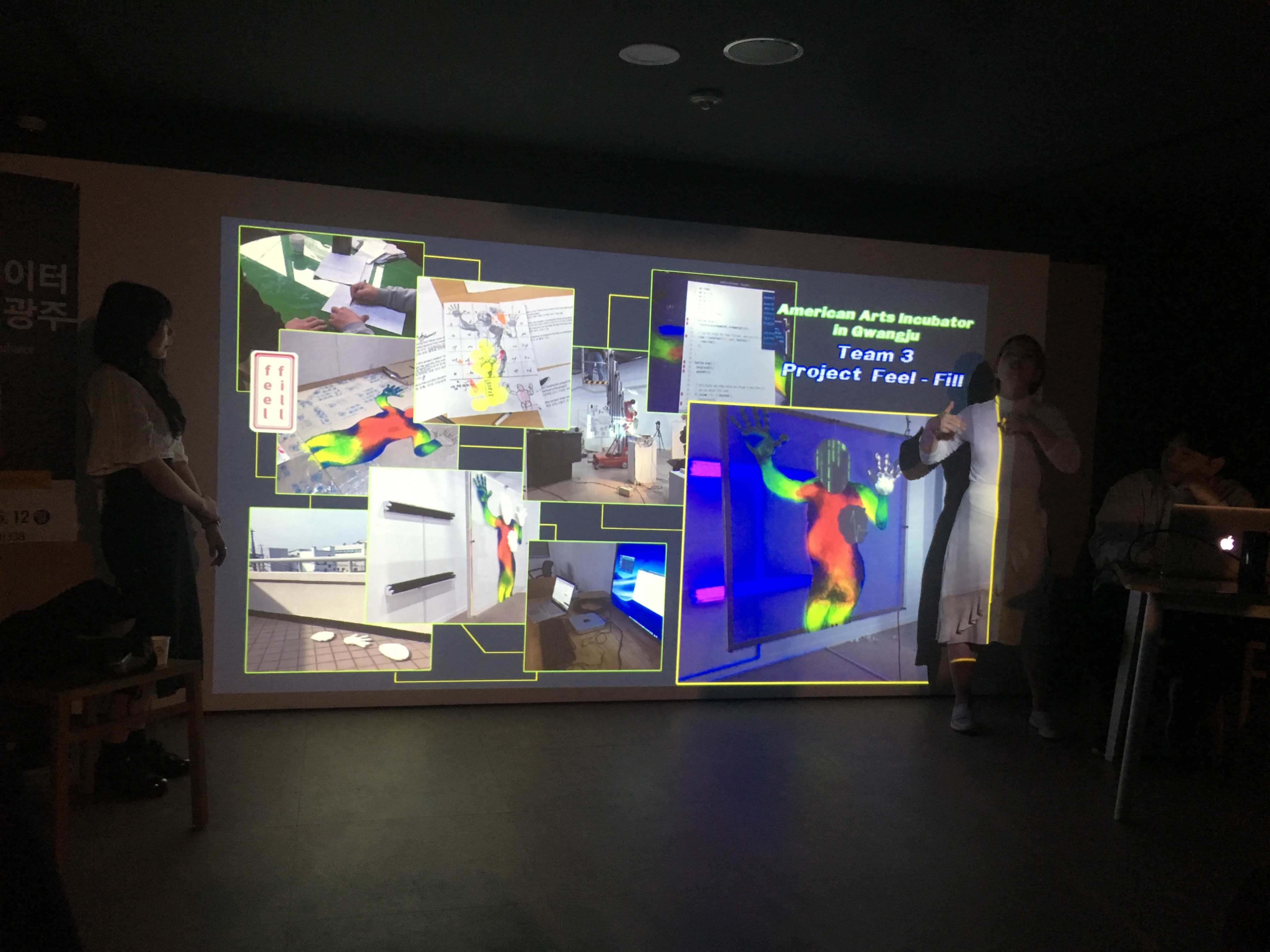 Two participants present in front of a projection of their work featuring bodies, colors, and sketches